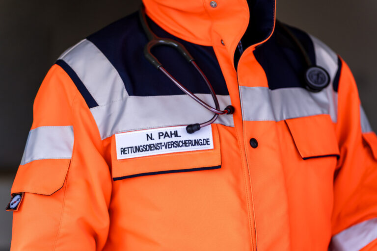 Oberkörper von Nikki Pahl in geschlossener oranger Einsatzjacke, Stethoskop um den Hals, Namensschild Rettungsdienst-Versicherung.de