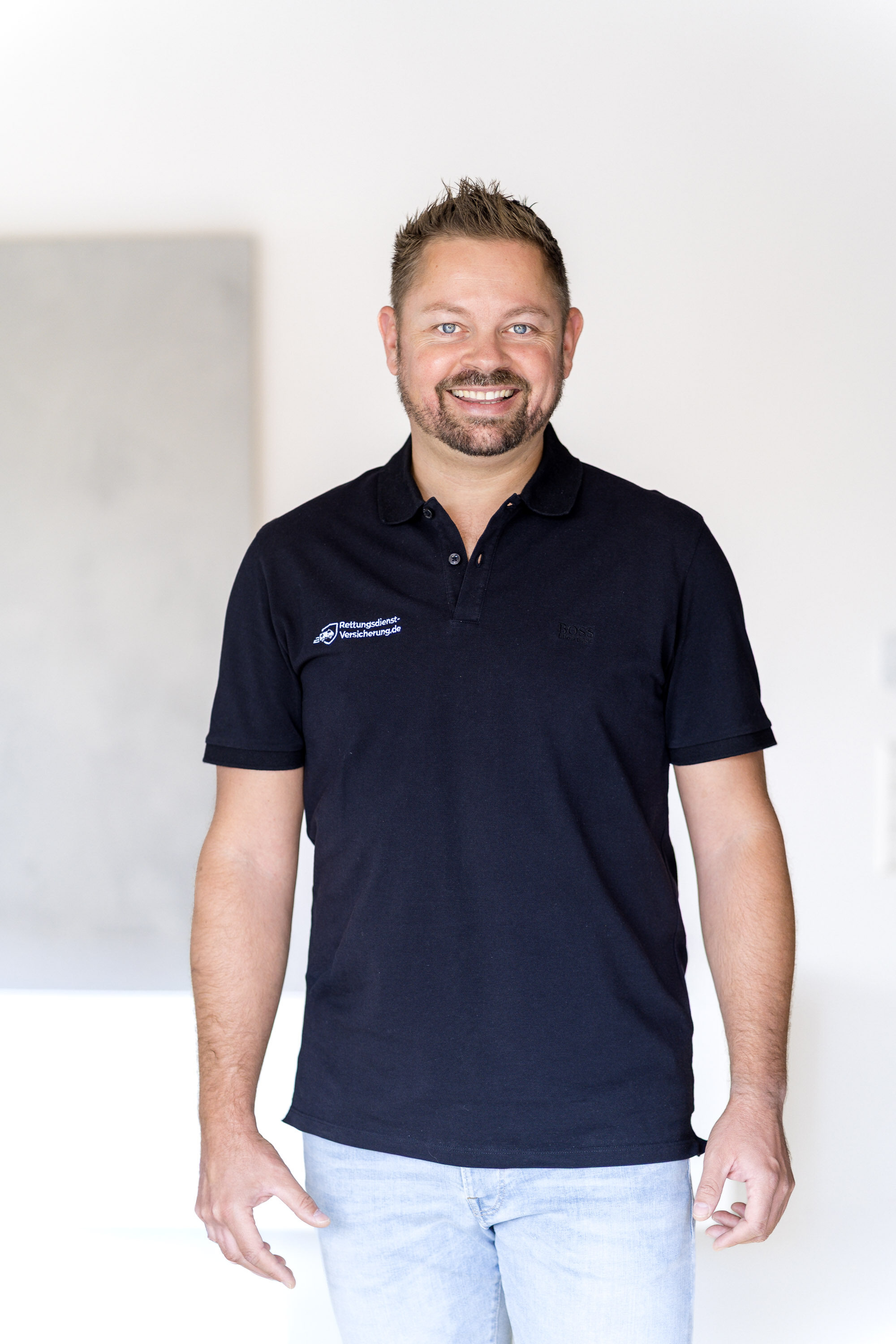 Nikki Pahl steht im schwarzen Poloshirt und Jeans vor einer hellen Wand und lächelt