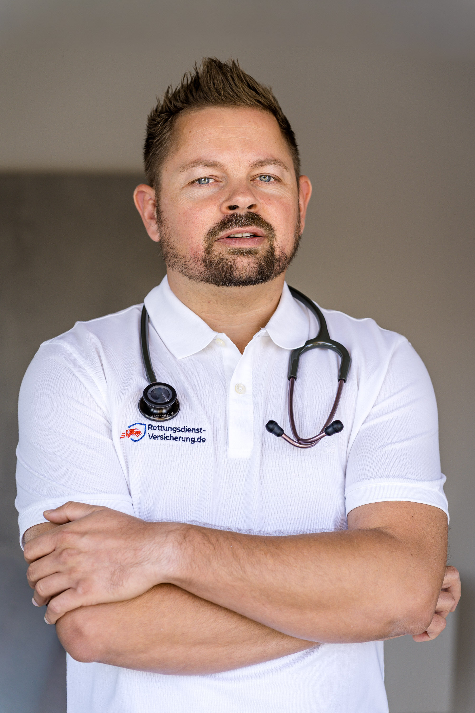 Nikki Pahl, Notfallsanitäter und Versicherungsmakler für die Berufsunfähigkeitsversicherung im Rettungsdienst, im weißen Polo mit Stethoskop und verschränkten Armen