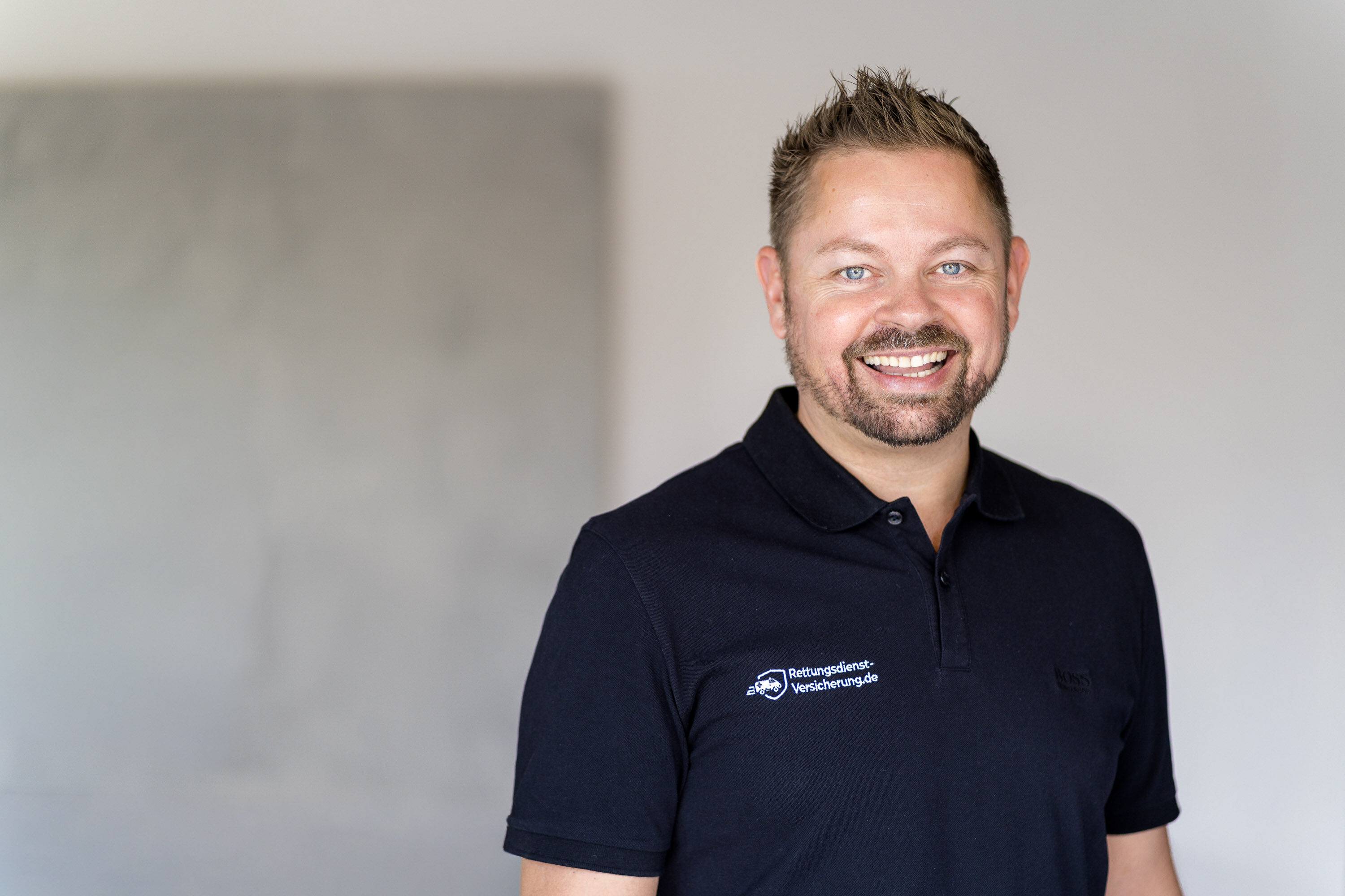 Nikki Pahl lacht in die Kamera, schwarzes Poloshirt mit Logo von Rettungsdienst-Versicherung.de